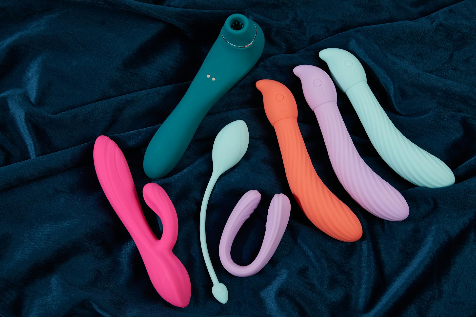 Assorted colorful silicone vibrators displayed on blue fabric background
