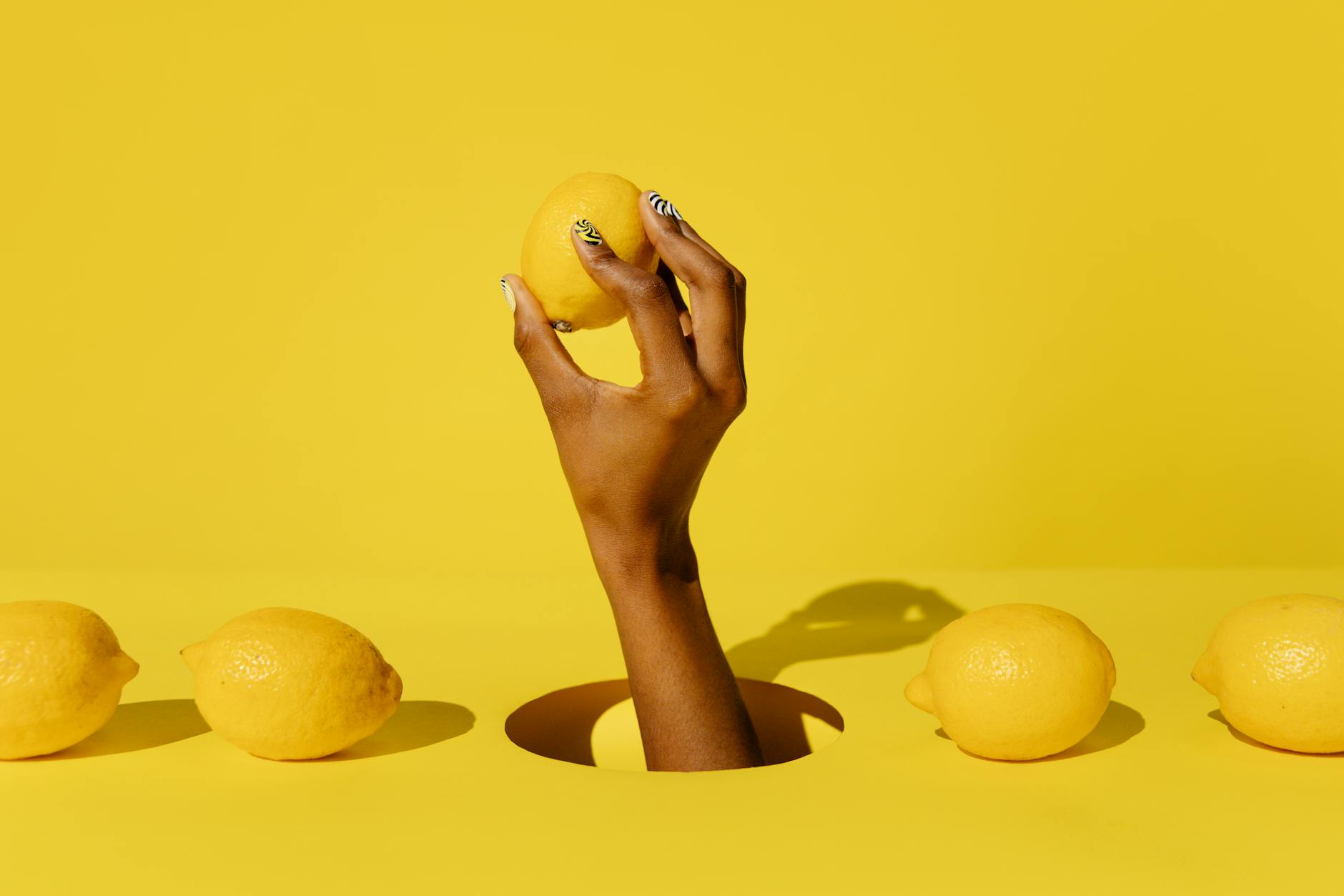 Una mano che regge un limone brillante su uno sfondo giallo vivace, simboleggiando freschezza e vitalità