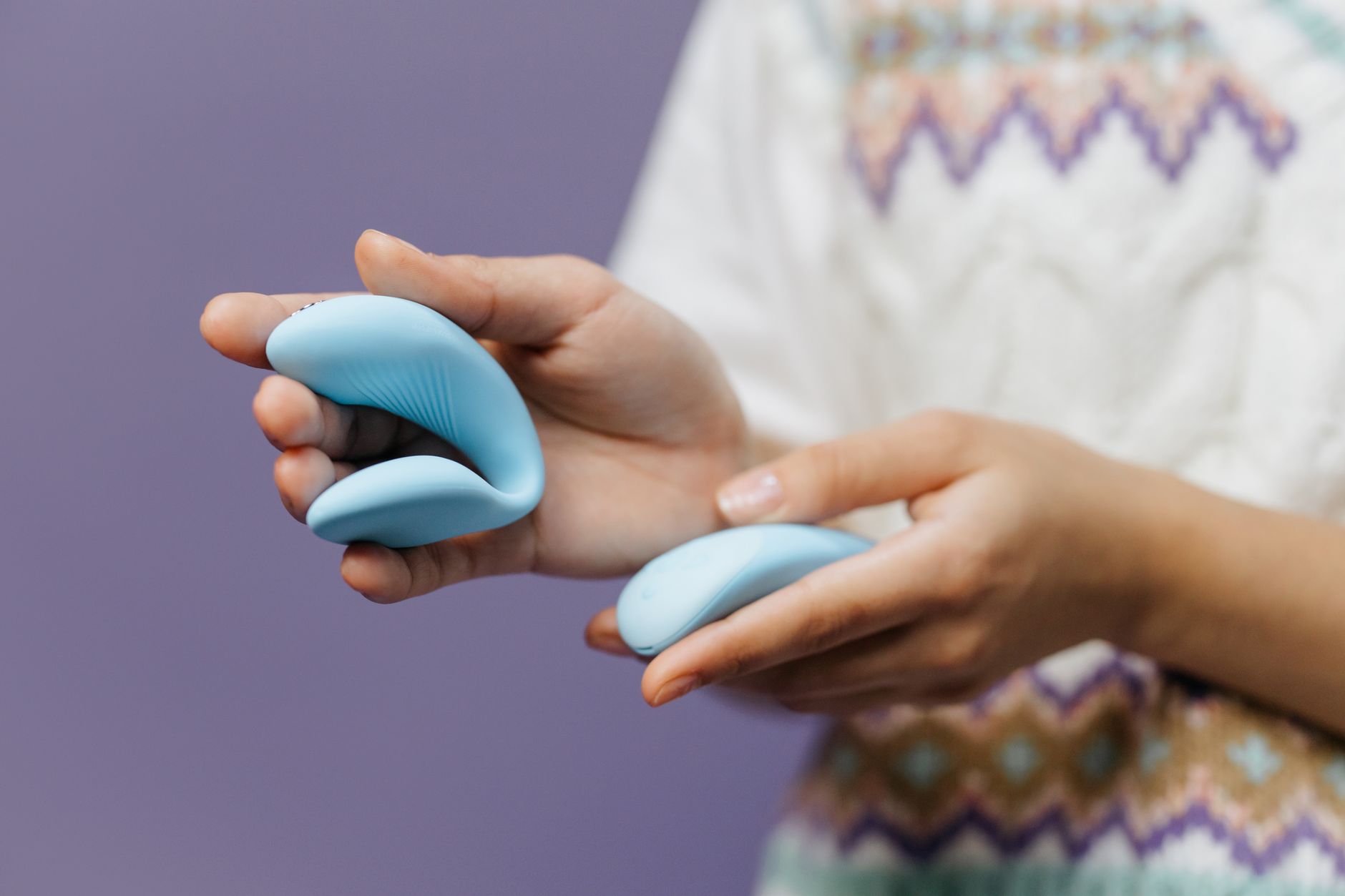 Mani che tengono un vibratore blu elegante contro uno sfondo viola, rappresentando il piacere intimo e consapevole