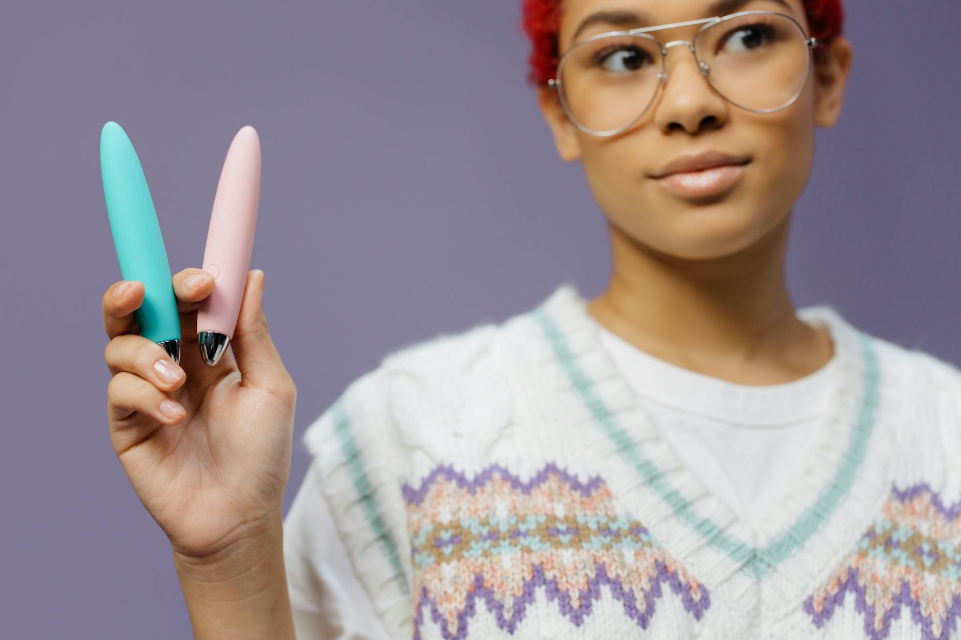A person holding colorful vibrators against a purple background, representing diverse sensation and pleasure options