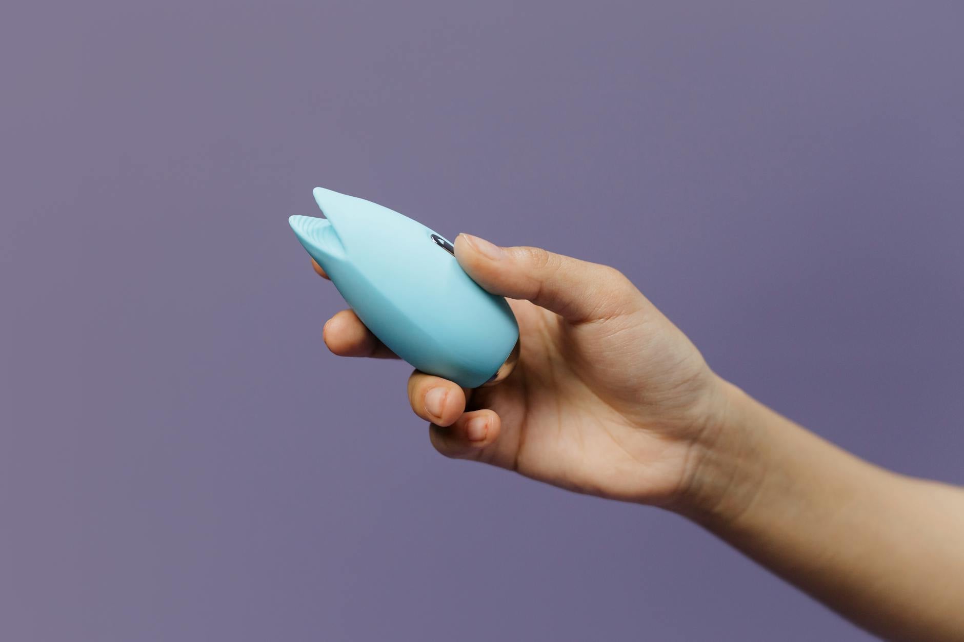 Mano che tiene un vibratore blu su sfondo viola, simbolo dell'amore per sé e della sessualità