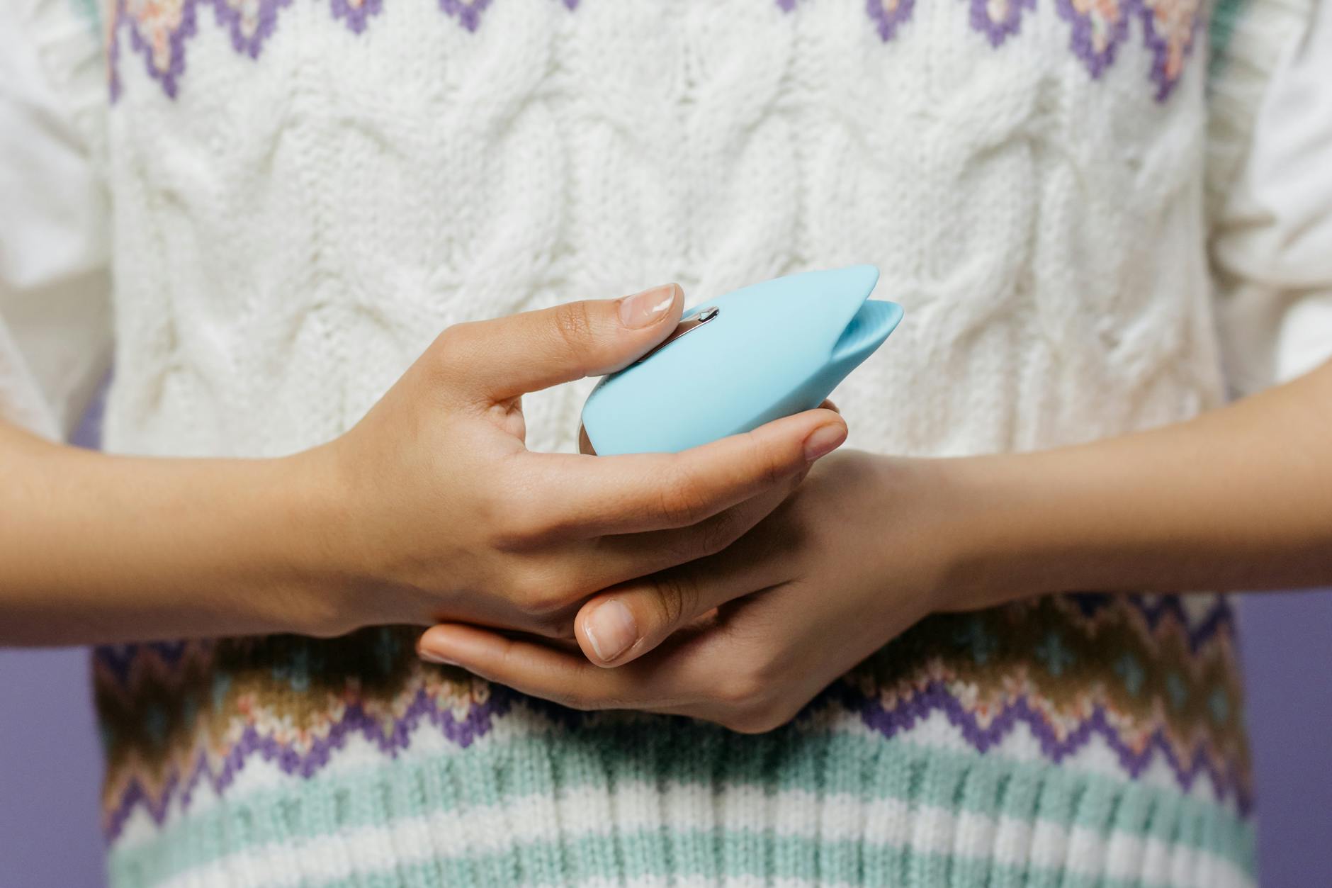 Two hands holding pink and blue silicone vibrators against a pastel background, representing shared intimacy.